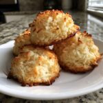 A stack of four golden brown, perfectly toasted chewy coconut cookies on a white plate.