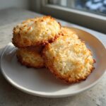 A stack of golden brown, chewy coconut cookies with toasted edges served on a white plate.