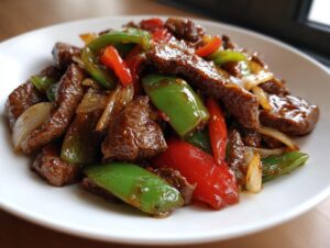A close-up of glossy, saucy chinese pepper steak with onions and peppers served on a white plate.