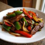 Close-up of savory Chinese pepper steak with onions and peppers served on a white plate.