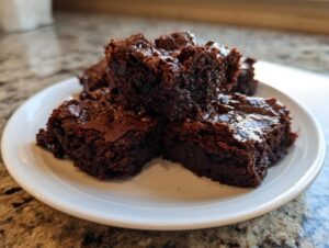 Close-up of several rich, fudgy chocolate date brownies stacked on a small white plate.