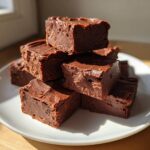 A stack of rich, dark chocolate peanut butter fudge recipe squares piled high on a white plate.