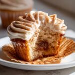 A close-up of a churro cupcake cut in half showing the cinnamon filling and cream cheese frosting.