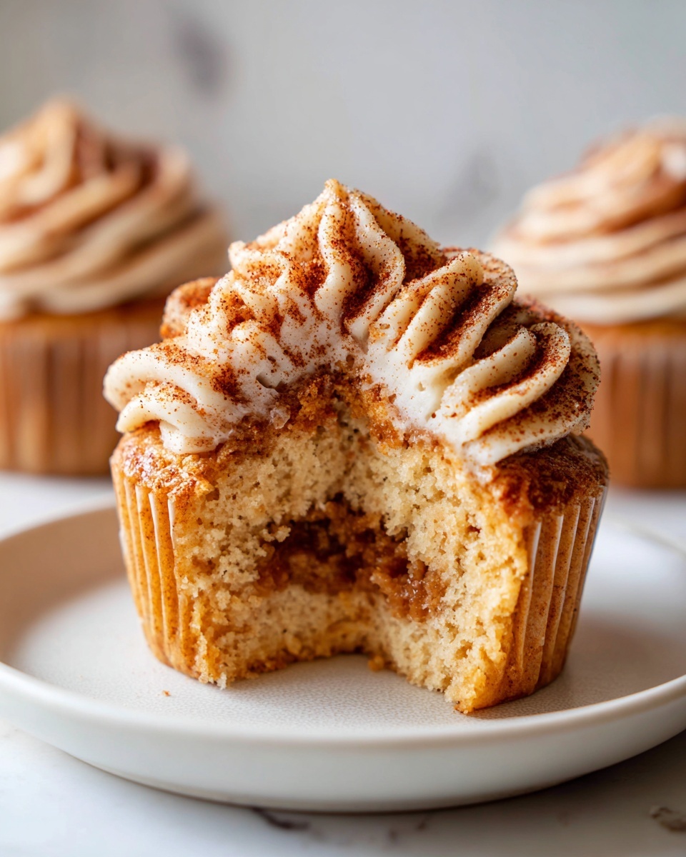 Close-up of a churro cupcake with a bite taken out, revealing a cinnamon filling and cinnamon-dusted frosting.