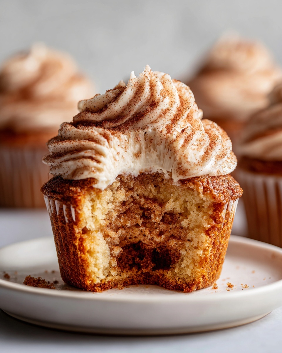 Close-up of a bitten churro cupcake showing the cinnamon swirl interior and cream cheese frosting topped with cinnamon sugar.