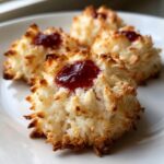 Close-up of freshly baked coconut macaroon blossoms topped with a dollop of red jam.