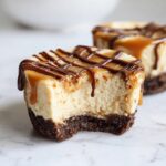 Close-up of a cookie butter cheesecake cup with a bite taken out, drizzled with caramel and chocolate sauce.