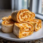 A stack of sliced cream cheese taco pinwheels showing the orange and white swirl filling on a white plate.