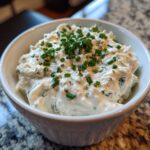 A close-up of creamy blue cheese dip topped generously with fresh, chopped green chives in a white bowl.
