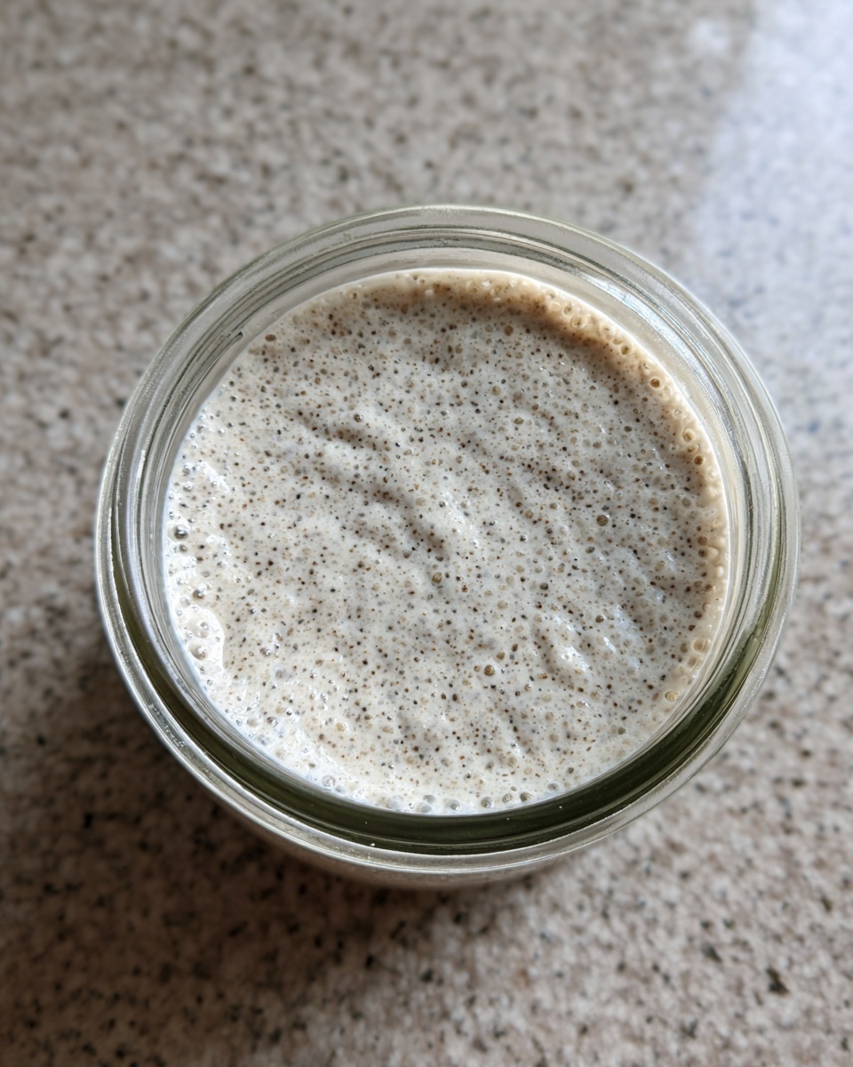 Overhead close-up of creamy, speckled chia pudding texture inside a clear glass jar.