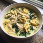 Close-up of a bowl of creamy chicken tortellini soup featuring shredded chicken, spinach, and cheese.