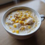 Close-up of a creamy crab and corn soup, featuring shredded crab meat and bright yellow corn kernels in a white bowl.