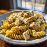 A close-up of creamy garlic chicken and rotini in parmesan sauce, featuring chunks of seasoned chicken over corkscrew pasta.