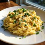 A serving of creamy, cheesy orzo pasta topped with fresh parsley and grated cheese.