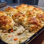 Close-up of a creamy chicken pot pie casserole topped with golden brown, fluffy biscuits.