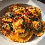 A close-up shot of delicious creamy Tuscan ravioli covered in a rich, orange-hued sauce with spinach and sun-dried tomatoes.