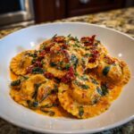 Close-up of Creamy Tuscan Ravioli with Sausage coated in an orange-hued sauce with spinach and sun-dried tomatoes.