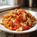Close-up of shredded chicken mixed with sliced red and yellow peppers, ready for crockpot chicken fajitas.