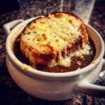 Close-up of a steaming bowl of crockpot french onion soup topped with a thick slice of toasted bread and melted, bubbly Gruyère cheese.