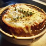 A close-up of crockpot french onion soup slow cooker topped with melted cheese, toasted bread, and thyme.