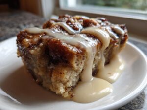 A close-up of a square serving of rich bread pudding topped with thick vanilla glaze.