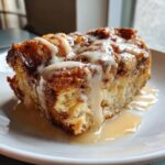 Close-up of a rich slice of bread pudding topped with thick vanilla glaze and caramel sauce.