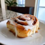 A close-up of one fluffy homemade cinnamon rolls topped generously with white cream cheese icing.