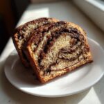 Two thick slices of gluten free cinnamon bread showing a rich, dark cinnamon swirl pattern on a white plate.