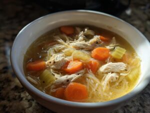 Close-up of a white bowl filled with gluten free slow cooker chicken noodle soup, featuring shredded chicken, carrots, and noodles.