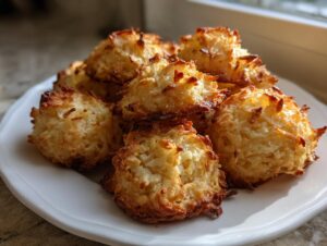 A pile of freshly baked, golden brown coconut macaroons with crispy edges on a white plate.