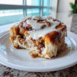 Close-up of a single, gooey tiktok cinnamon roll topped generously with white cream cheese frosting.
