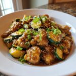 A close-up of a serving of ground chicken zucchini stir fry coated in a savory sauce, topped with sesame seeds and green onions.