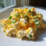 Close-up of a scoop of creamy healthy jalapeno popper chicken salad topped with shredded cheddar and green onions.