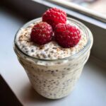 Close-up of high protein chia pudding in a glass jar topped with three fresh raspberries and cinnamon.
