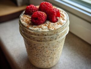 Close-up of a jar filled with creamy high protein chia pudding, topped with fresh raspberries and cinnamon.