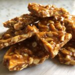 Close-up of broken, glossy pieces of homemade peanut brittle recipe stacked together.