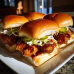 Four delicious hot honey chicken sliders stacked with crispy chicken, slaw, and pickles on brioche buns.