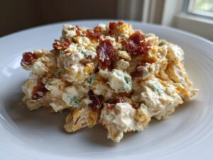 A scoop of creamy jalapeno popper chicken salad high protein topped with crispy bacon crumbles on a white plate.