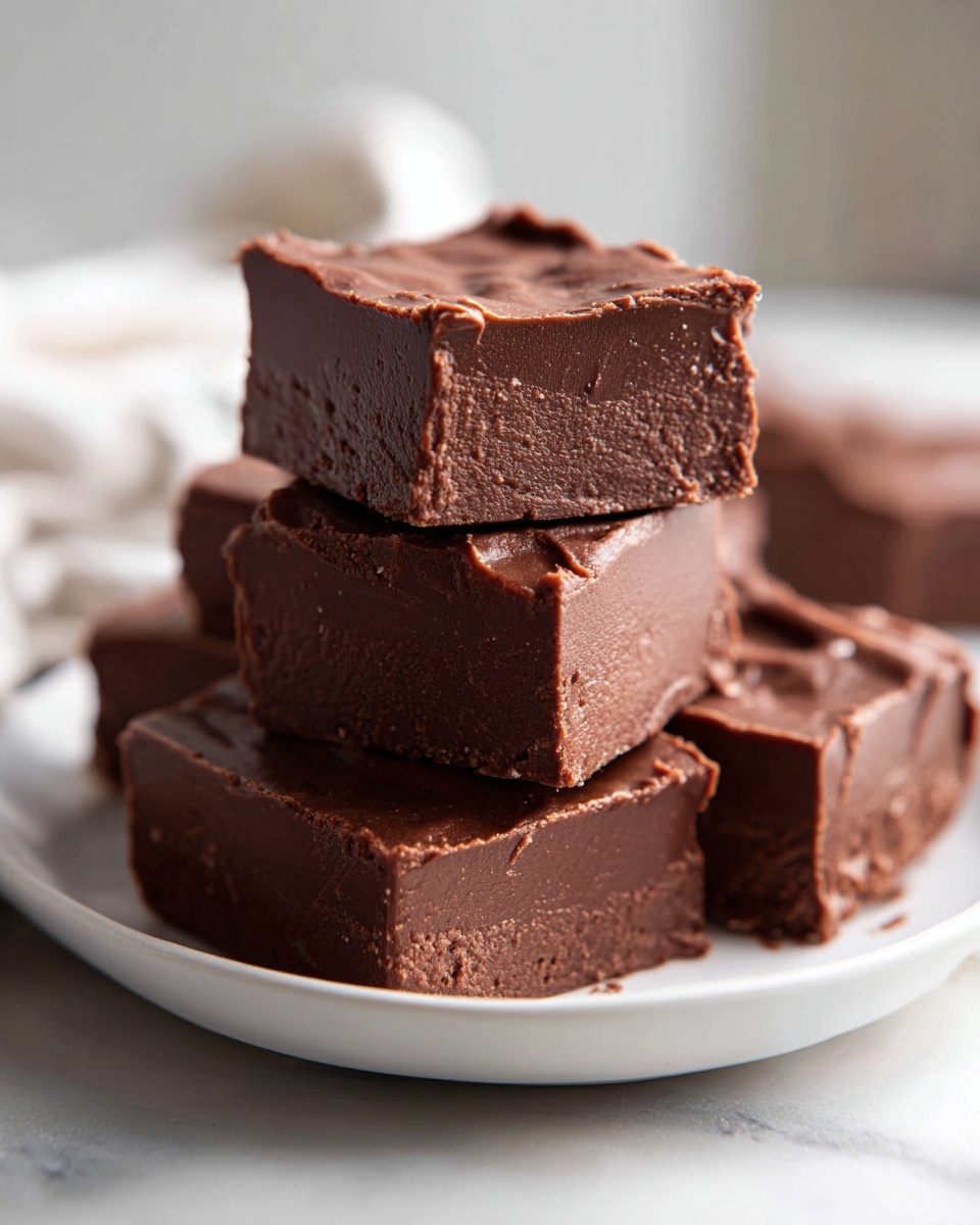 A stack of rich, dark squares of keto chocolate peanut butter fudge resting on a white plate.