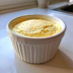 A single serving of fluffy, yellow keto egg custard baked in a white, ribbed ramekin dish.