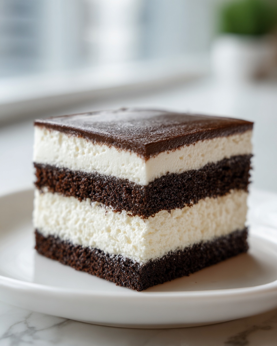 A square slice of layered chocolate and cream cake, reminiscent of an italian love cake, on a white plate.