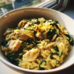 A close-up of creamy lemon chicken orzo pasta mixed with spinach and topped with bright yellow lemon zest.