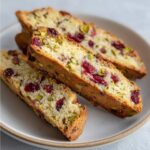 Close-up of three slices of lemon cranberry pistachio biscotti featuring bright red cranberries and green pistachios.