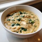 Close-up of a hearty bowl of marry me chicken orzo soup with shredded chicken and wilted spinach.