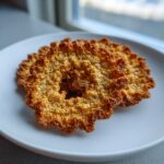 Close-up of two crispy, golden brown oatmeal lace cookies resting on a simple white plate.