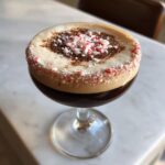 A close-up of a peppermint espresso martini with a thick foam top, rimmed with crushed candy canes.