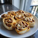A white plate holding several baked taco pinwheels filled with seasoned ground meat and melted cheese.