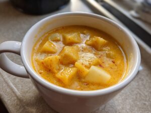 Close-up of creamy, orange-yellow potato chunks in a rich cheese soup served in a white mug.