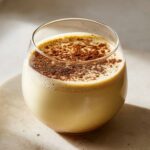 Close-up of a creamy glass of homemade eggnog, generously dusted with ground nutmeg or cinnamon.