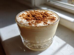 Close-up of a glass of creamy, homemade eggnog topped generously with ground cinnamon.